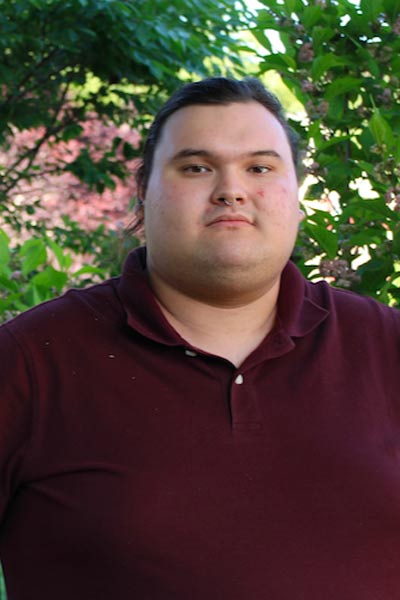 A three quarter informal portrait of a young man outside under a tree