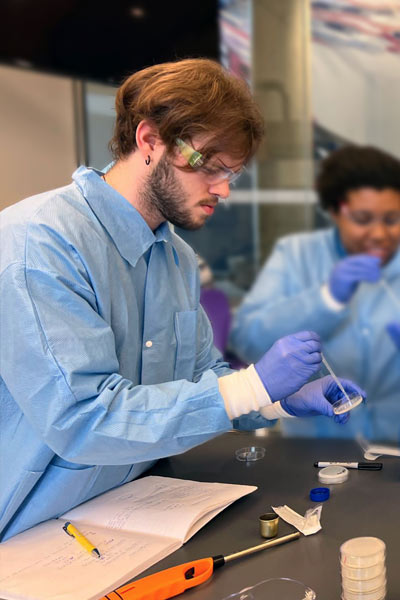 A young researcher in a biology lab taking a sample from a petri dish