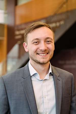 A professionally dressed man standing casually in a lobby of a building.