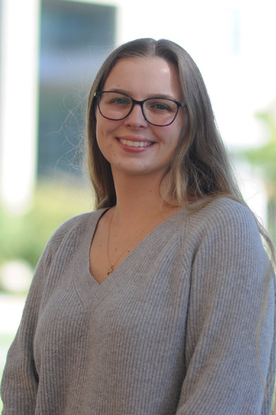 A young woman smiling while standing alone outside in a courtyard on campus