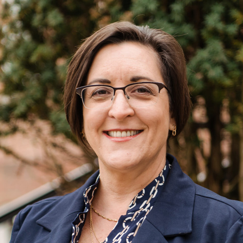 A smiling woman with glasses standing in a courtyard..